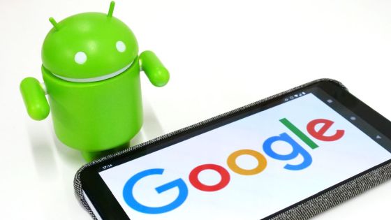 adroid robot standing by a phone with google on the screen